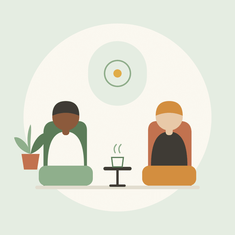 Two people sitting in armchairs with cups of tea on a small table between them.